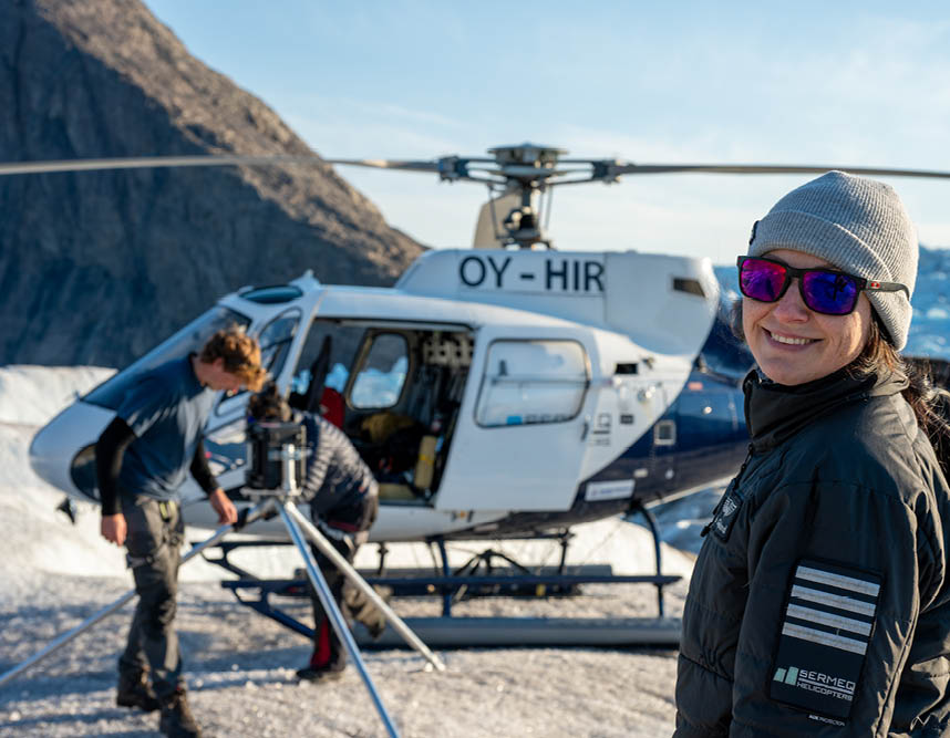 A woman wearing a black jacket and sunglasses is standing next to a helicopter. AI generated content