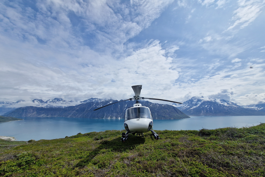 A white helicopter is parked on a grassy hillside overlooking a large body of water. AI generated content
