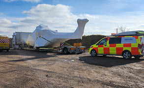 A white truck is parked next to a van in a parking lot. The truck is covered in plastic, and there is a large white object on the back of it. The van is parked in front of the truck, and there is a person standing nearby. AI generated content