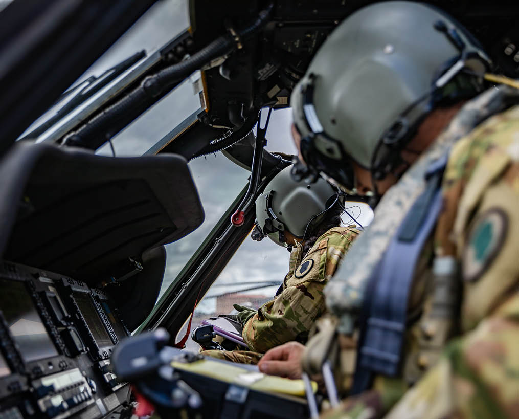 Two men wearing helmets and camouflage are sitting in a helicopter. AI generated content