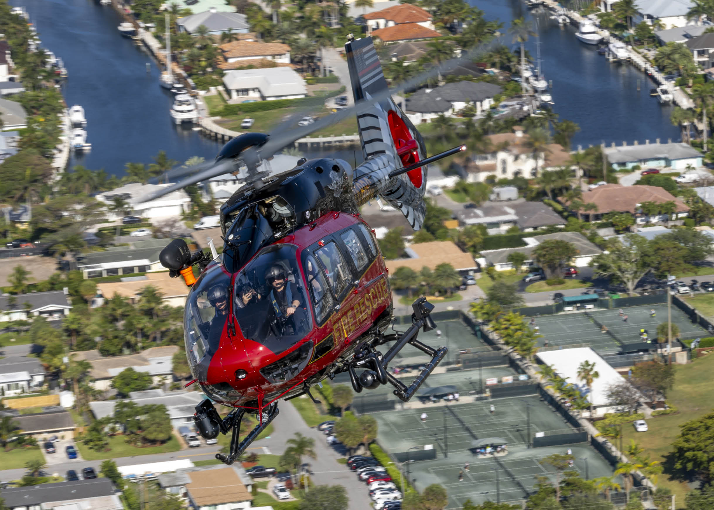 A red and white helicopter is flying over a neighborhood with houses and cars below. AI generated content