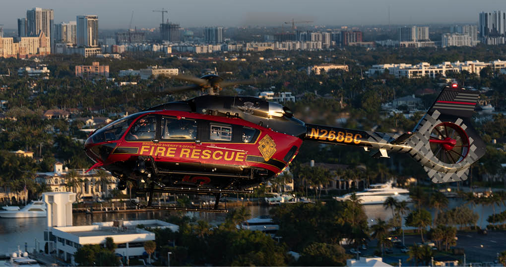 A red and yellow helicopter is flying over a city with a large building in the background. AI generated content