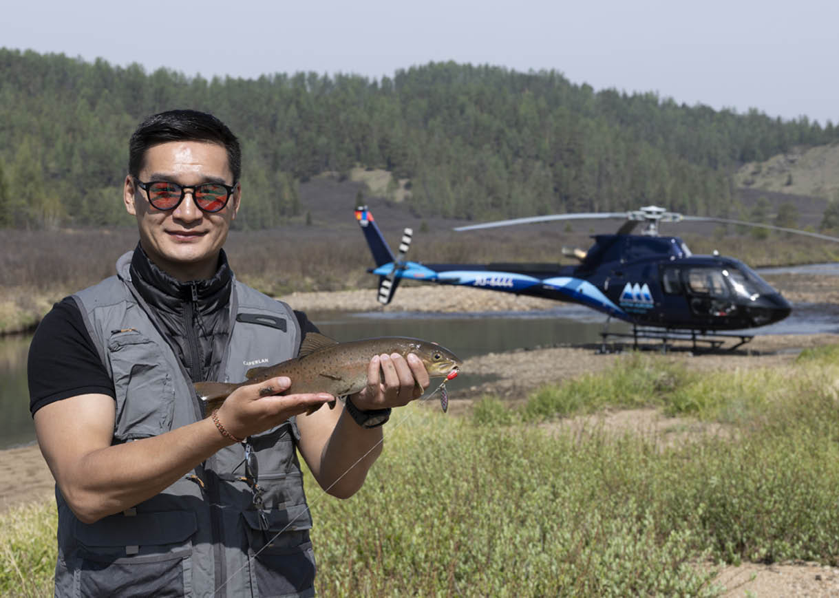 A man is holding a fish in his hand while standing next to a helicopter. AI generated content