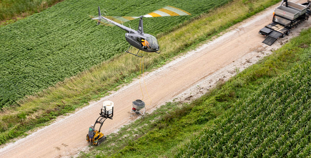 A helicopter is flying over a dirt road with a tractor on it. AI generated content
