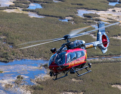 A red and yellow helicopter is flying over a field. AI generated content