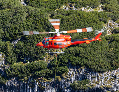 A red helicopter is flying over a rocky hillside with green trees. AI generated content
