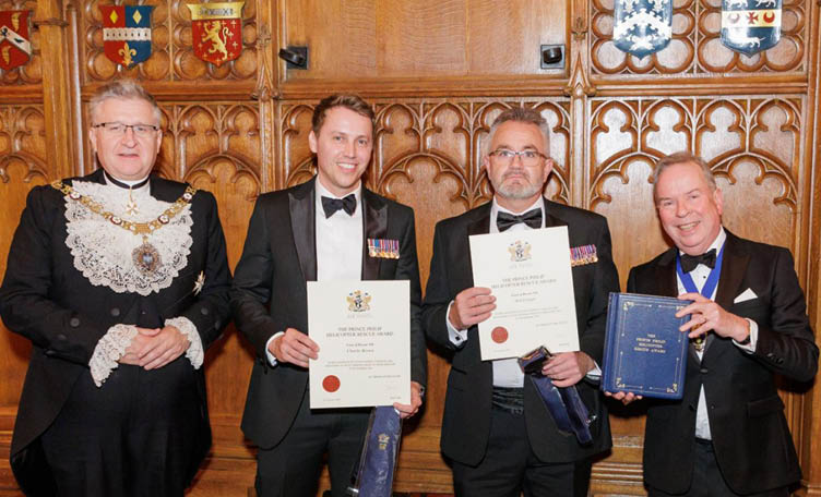 Three men in suits are holding awards, with one of them wearing a bow tie. They are standing in front of a man in a suit and tie, who is holding a book. The men are smiling for the camera. AI generated content