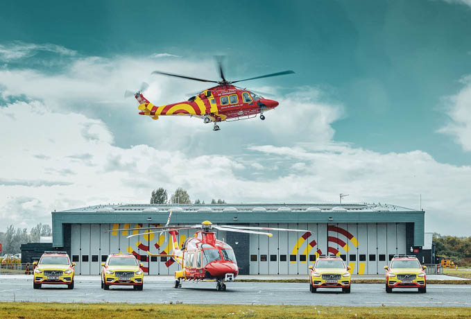 A red and yellow helicopter is flying over a parking lot with several cars parked. AI generated content