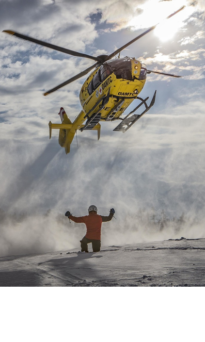 A man is standing in the snow, watching a yellow helicopter flying above him. AI generated content