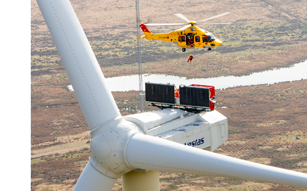 A yellow helicopter is flying over a windmill with a man hanging from a cable. AI generated content