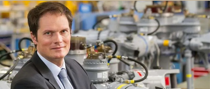 A man in a suit stands in front of a row of machinery. AI generated content