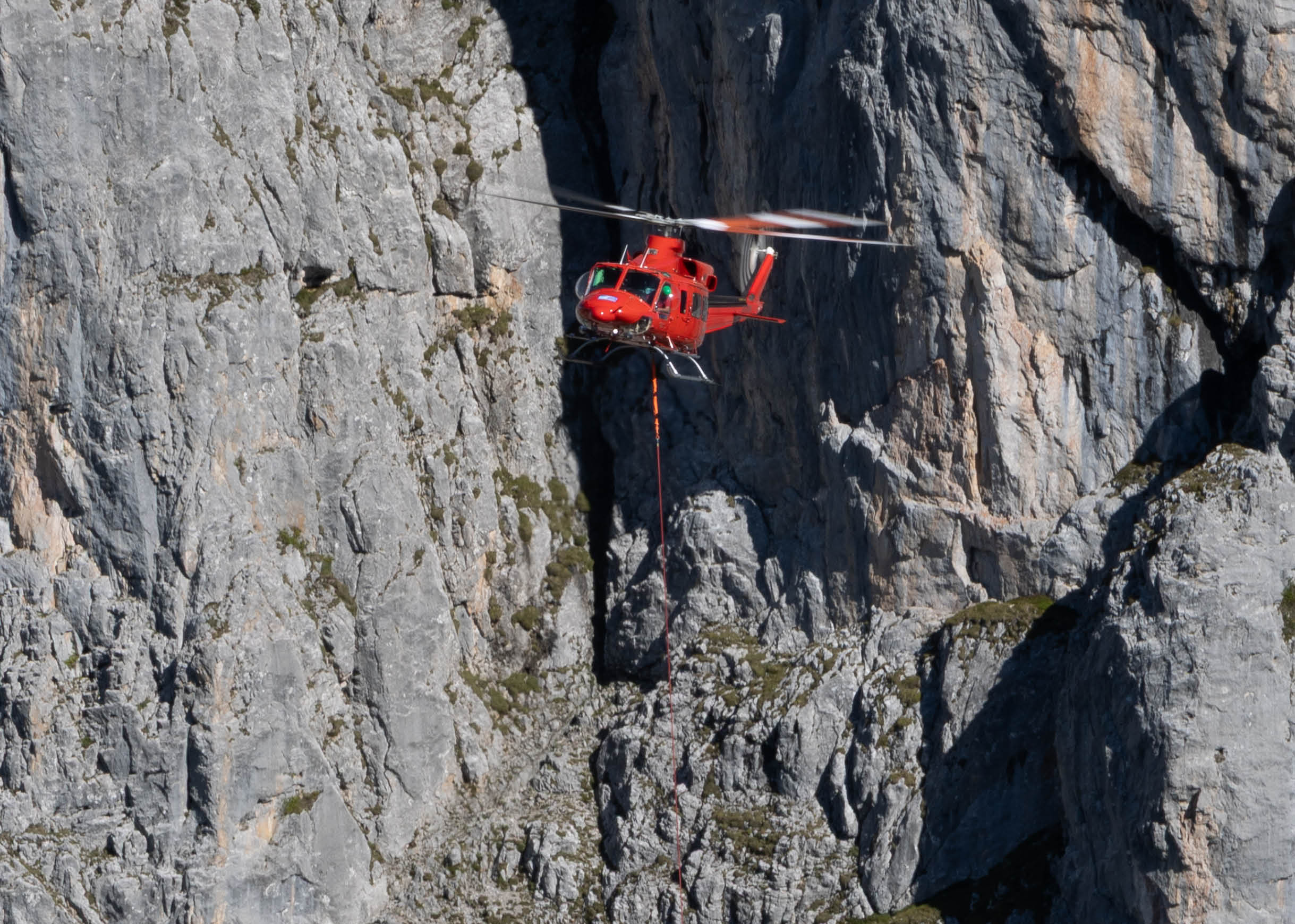 A helicopter is flying over a rocky cliff, with a person hanging from a rope below it. AI generated content