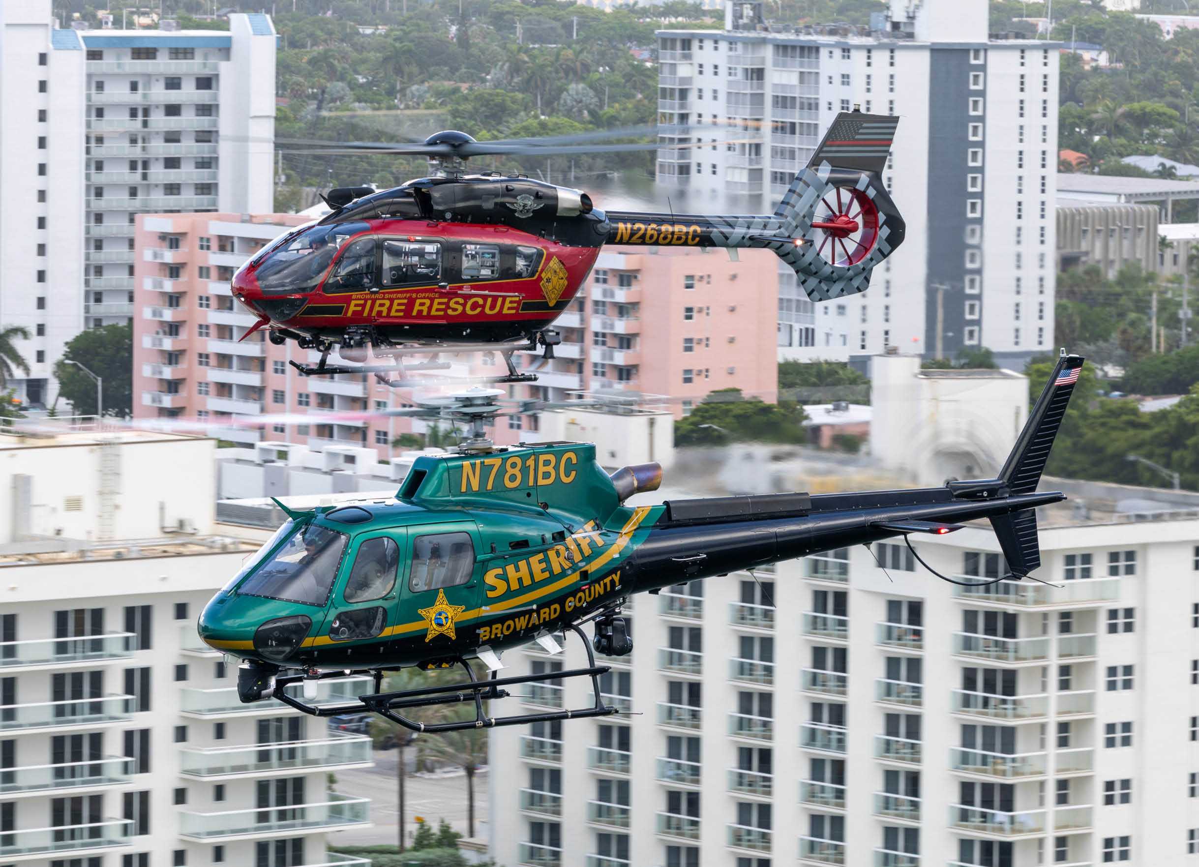 Two helicopters are flying over a city, one is green and the other is red. AI generated content