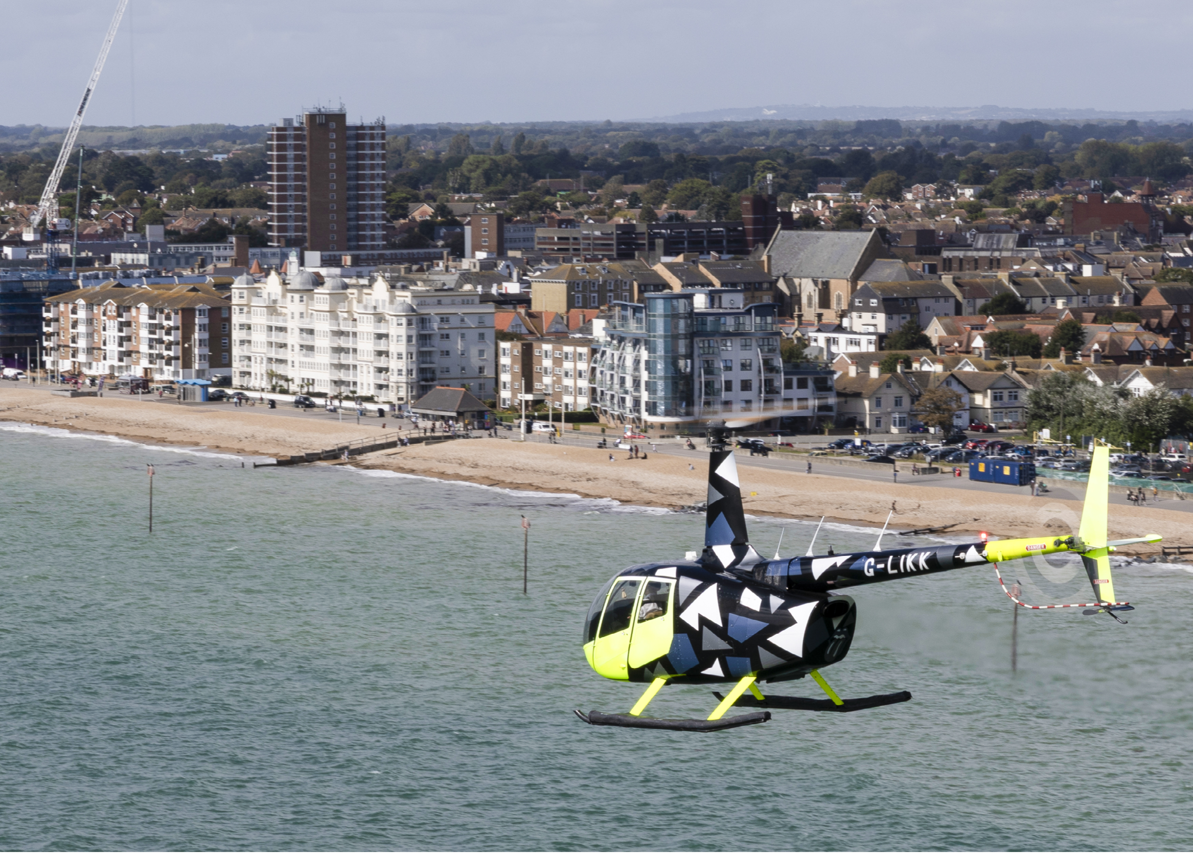 A yellow and black helicopter is flying over a beach. AI generated content