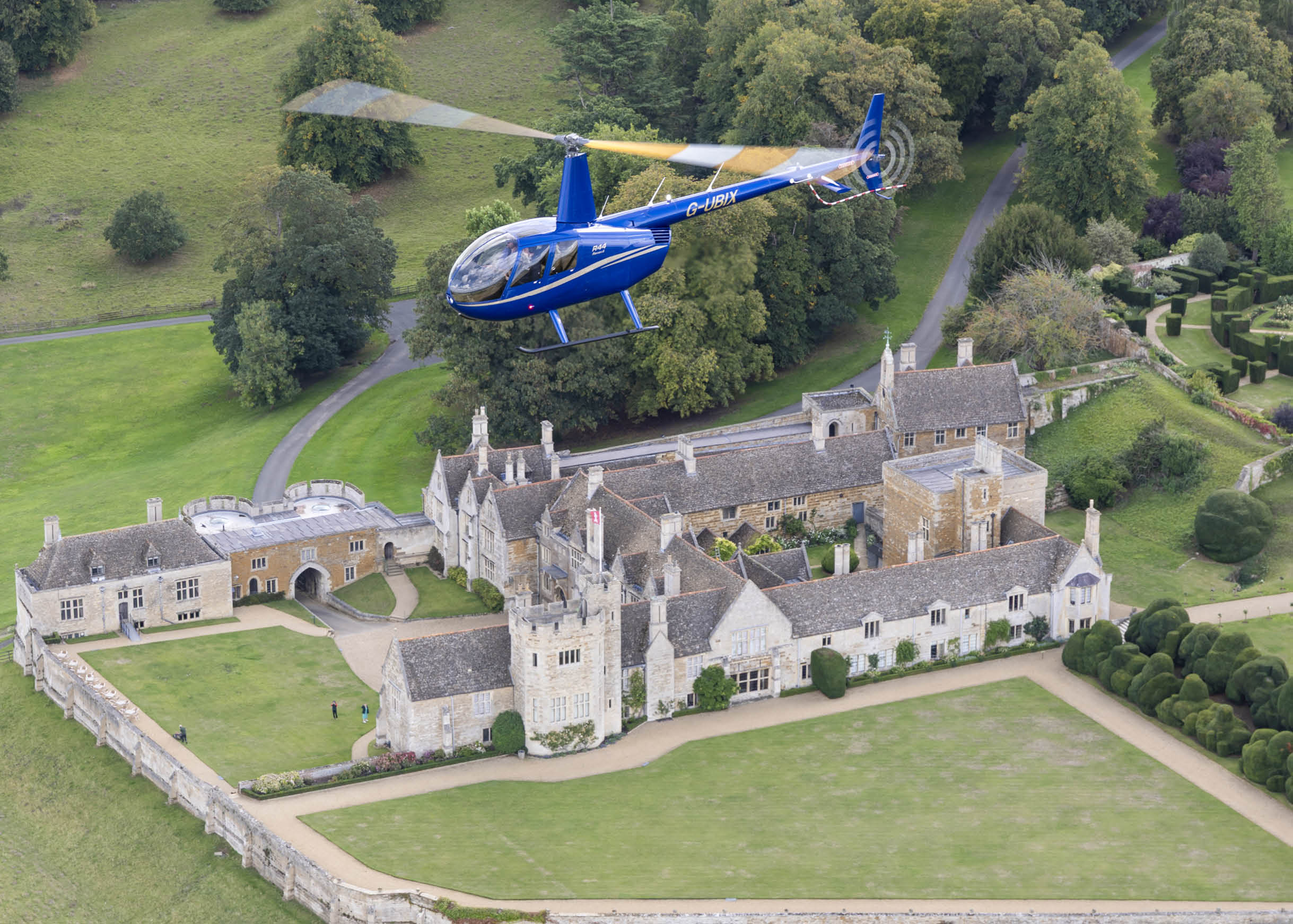 A blue and yellow helicopter is flying over a large house with a green lawn. AI generated content