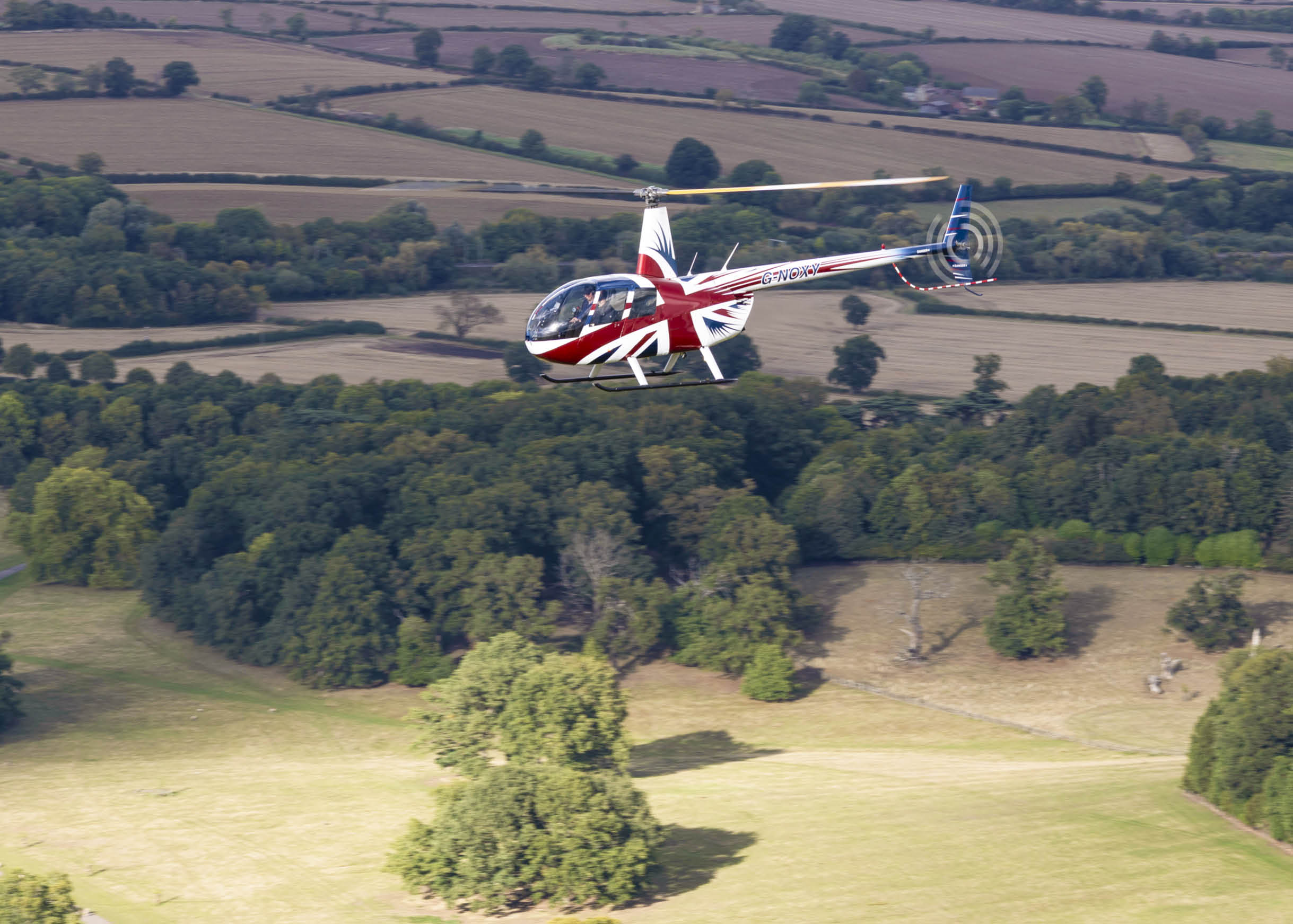 A red and white helicopter is flying over a field with trees in the background. AI generated content