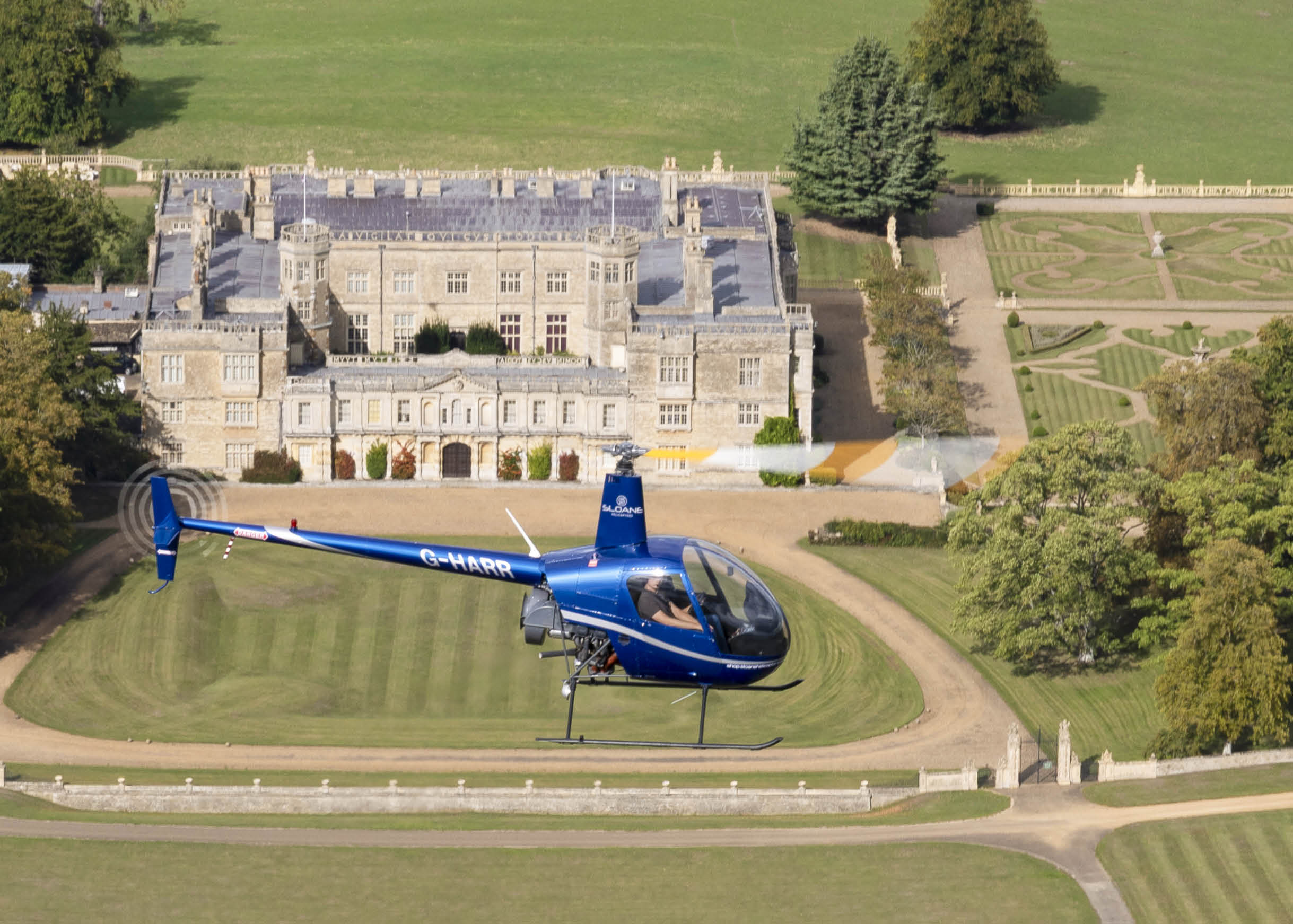 A blue helicopter is parked on a grassy field in front of a large house. AI generated content