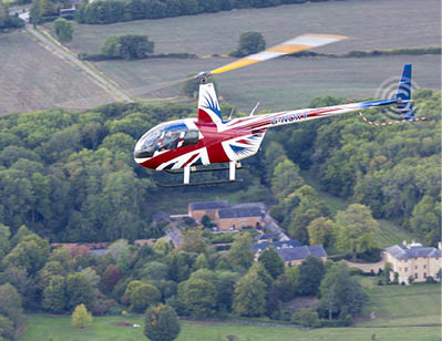 A red and white helicopter with a British flag on it is flying over a field. AI generated content