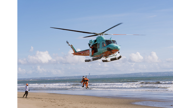A helicopter is flying over a beach with a person in orange and white. AI generated content