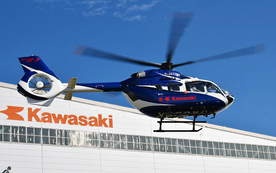 A blue and white helicopter is flying above a building with the word “Kawasaki" on it. AI generated content