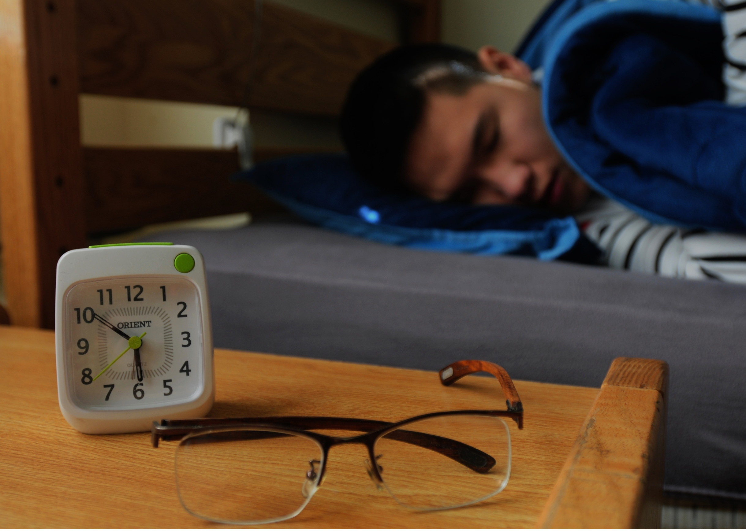 A man is sleeping on a bed with a clock and glasses on the nightstand. AI generated content