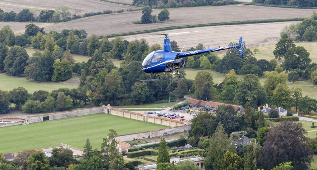 A blue helicopter is flying over a field with a house and cars below. AI generated content