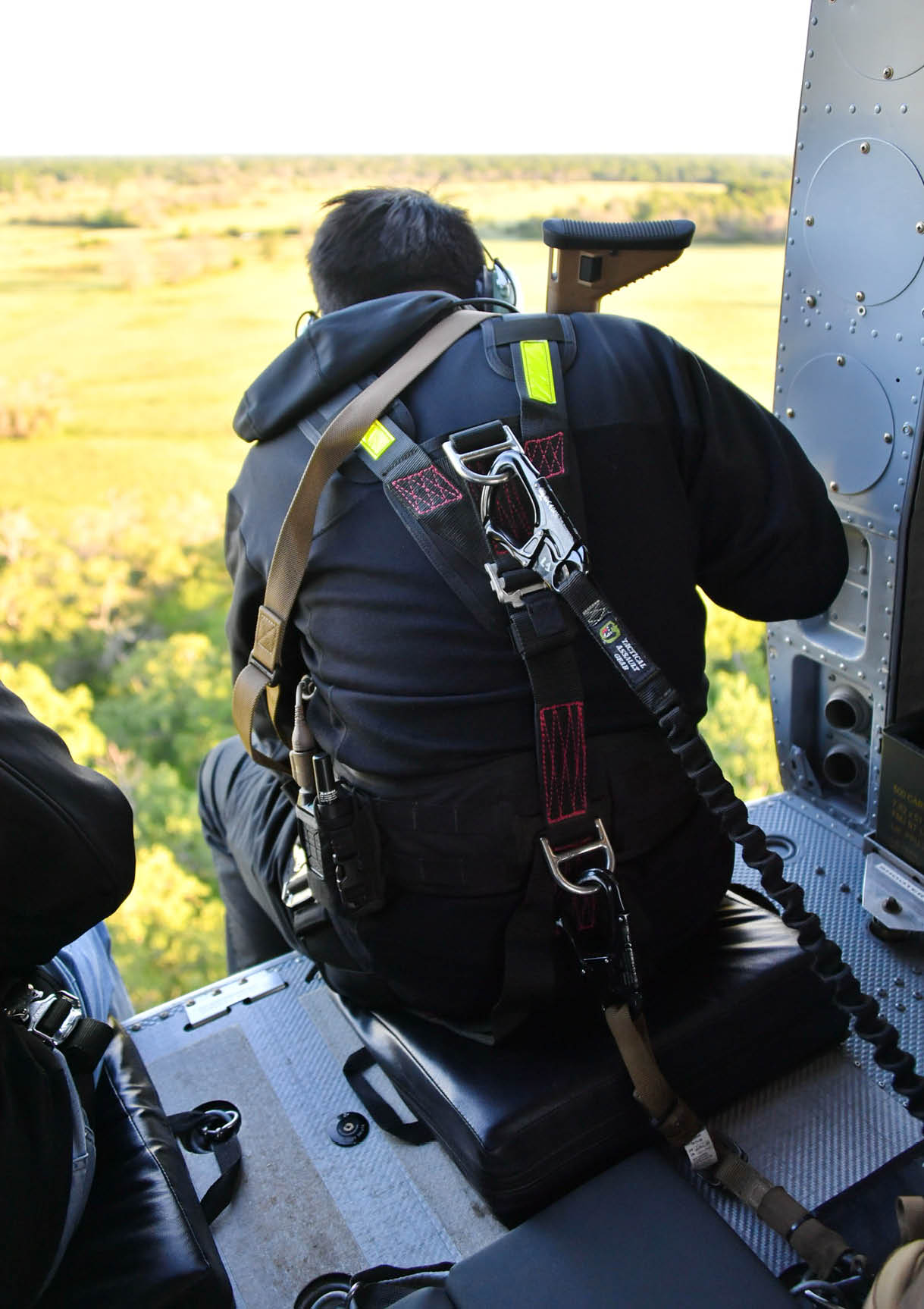 A man is sitting in a helicopter, wearing a harness and goggles. AI generated content