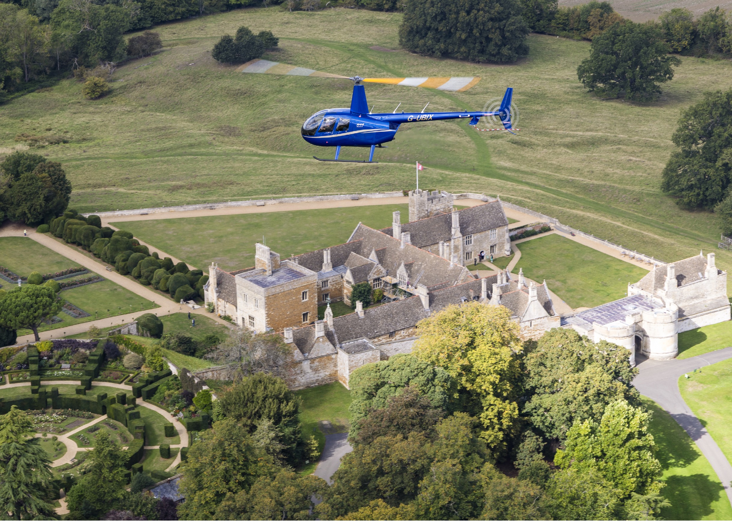 A blue helicopter is flying over a large mansion with a castle-like appearance. AI generated content