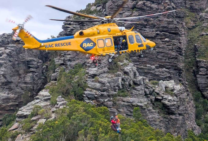 A yellow and blue helicopter flying over a mountain. Description generated by AI