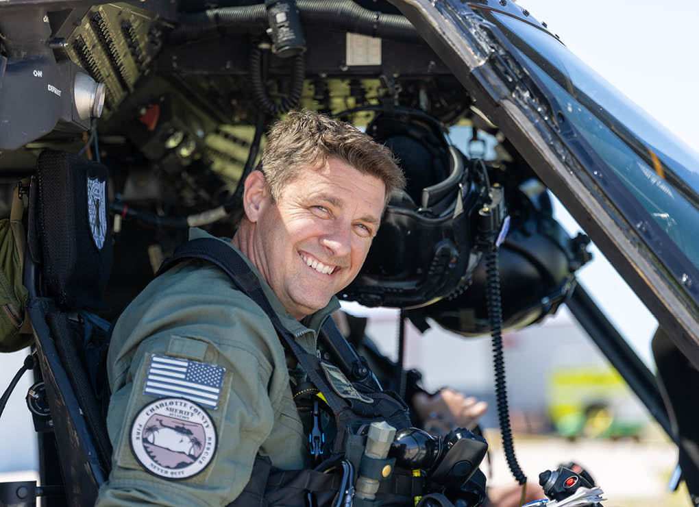 A man wearing a green shirt and a helmet is sitting in a helicopter. Description generated by AI