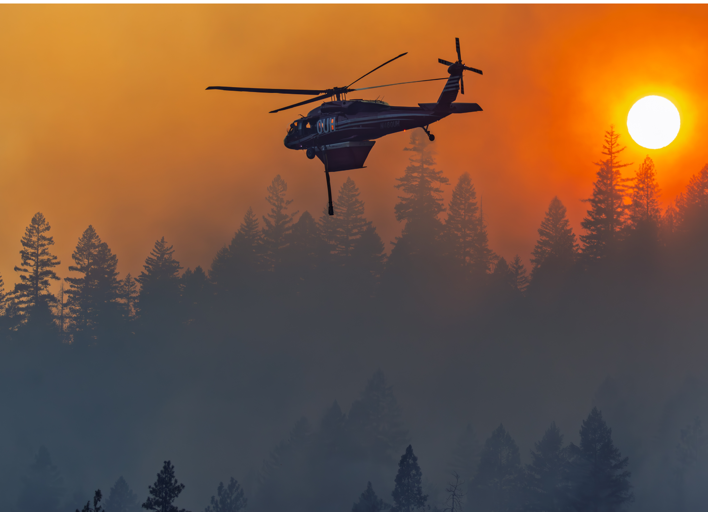 A helicopter flying over a forest during a sunset. Description generated by AI