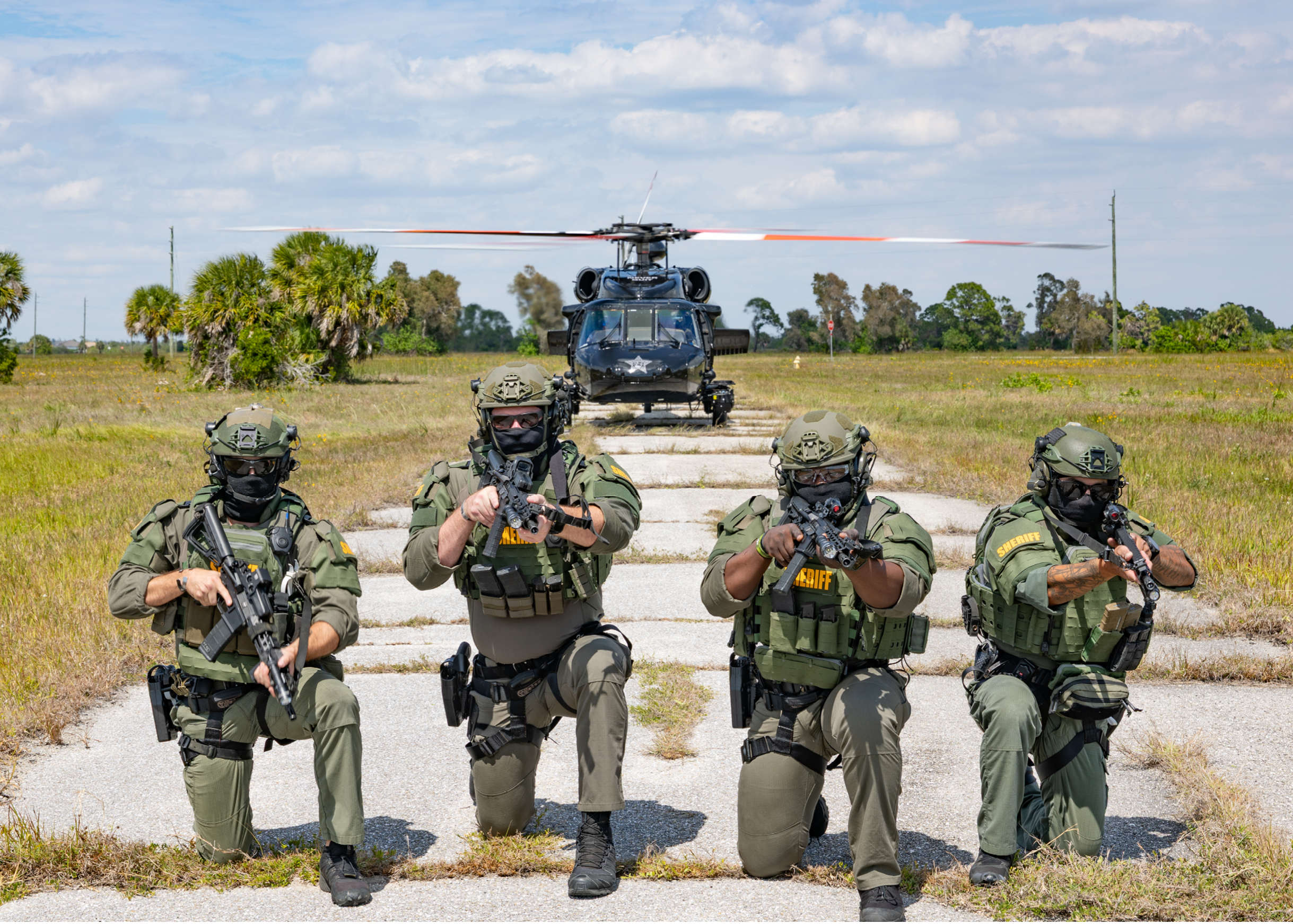 Four men in camouflage uniforms are kneeling on a road. Description generated by AI