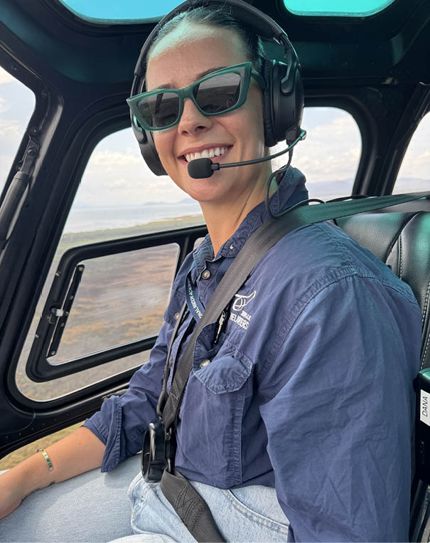 A woman wearing a blue shirt and sunglasses is sitting in a helicopter. Description generated by AI