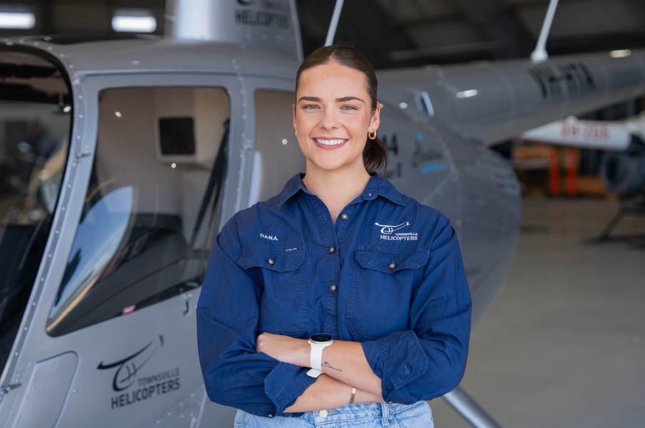 A woman in a blue shirt and jeans standing in front of a helicopter. Description generated by AI