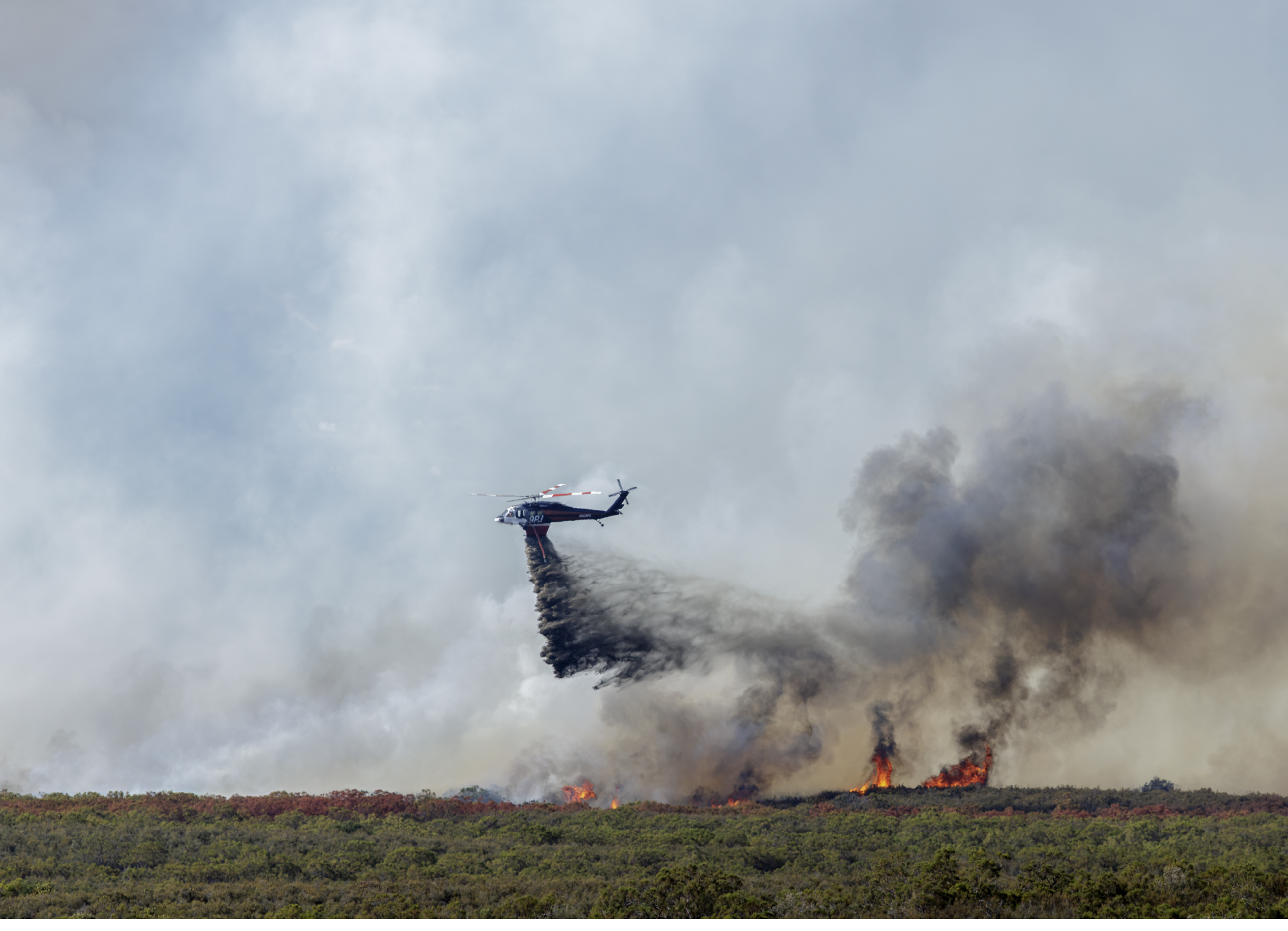 A helicopter is flying through a smoke filled sky. Description generated by AI