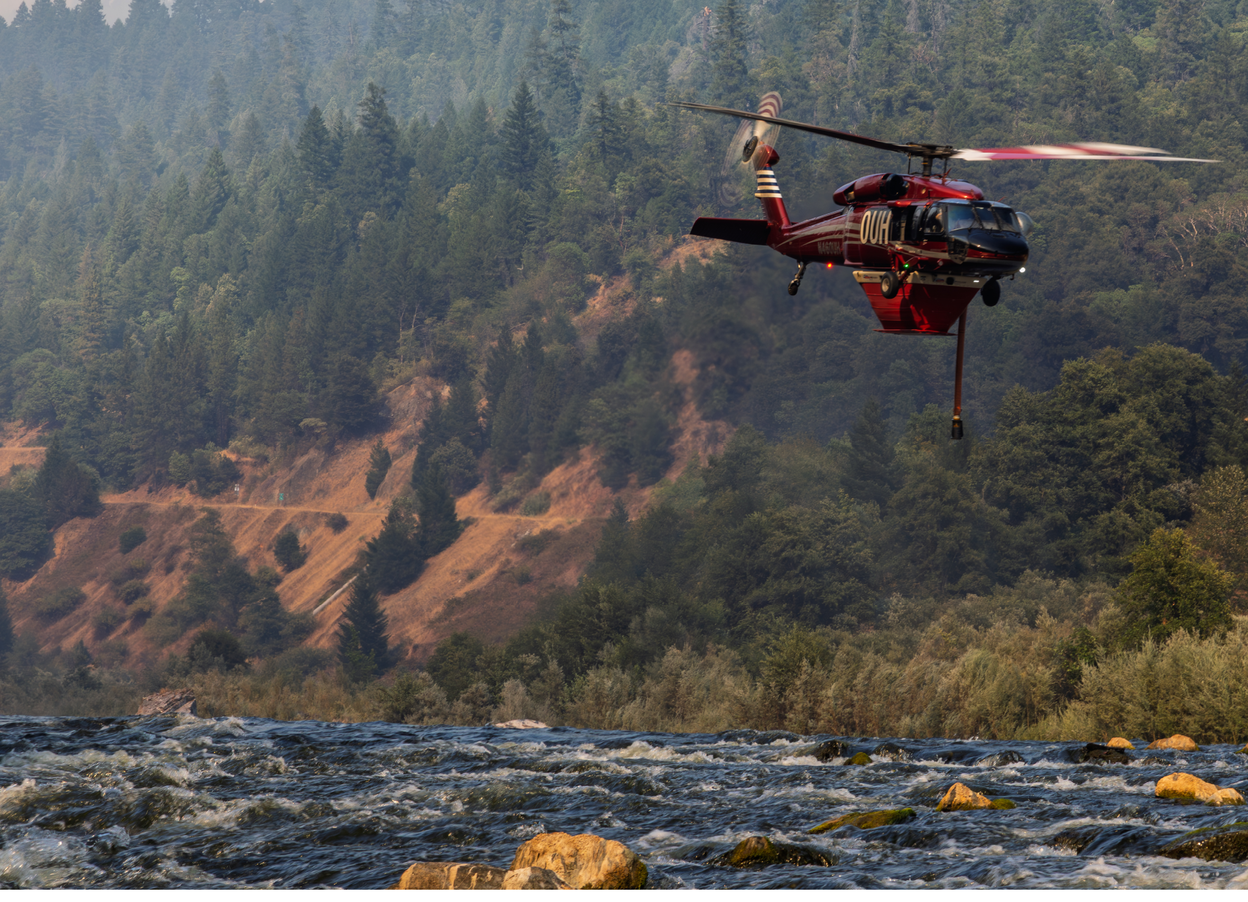 A red helicopter is flying over a river. Description generated by AI