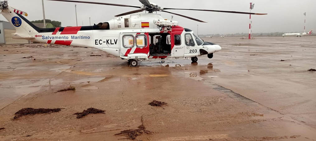 A red and white helicopter is parked on a wet tarmac. Description generated by AI