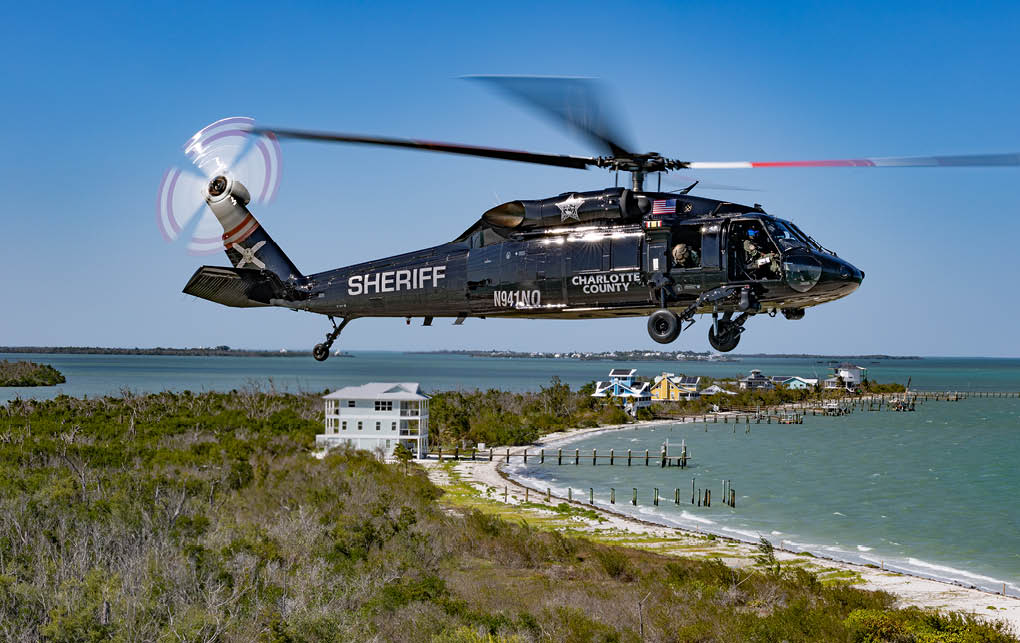 A helicopter flying over a beach. Description generated by AI