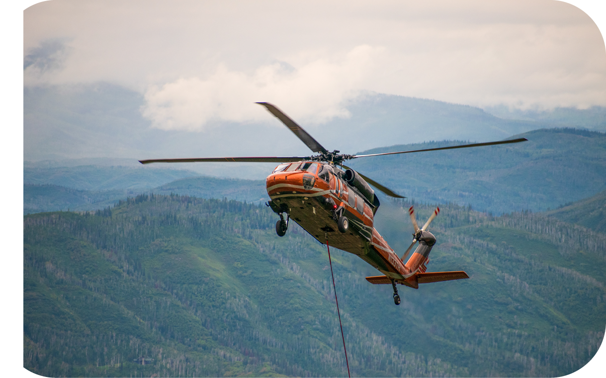 A helicopter is flying in the air with a rope hanging from it. Description generated by AI