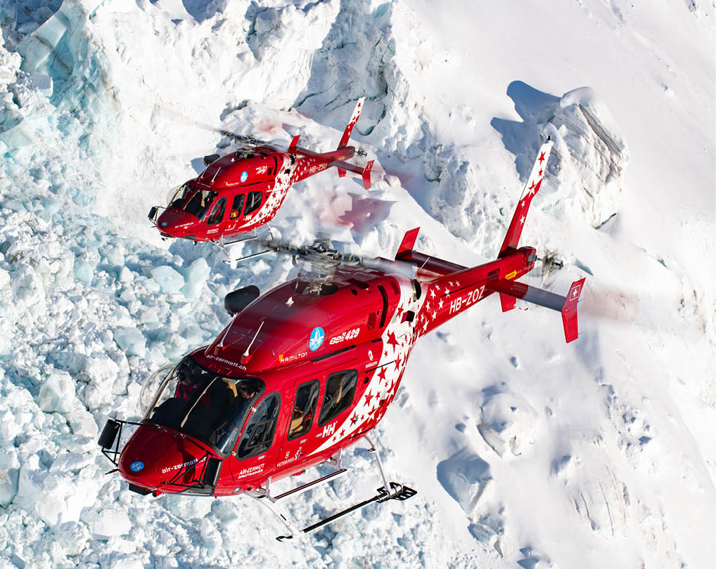 Two red helicopters flying over a snowy mountain. Description generated by AI