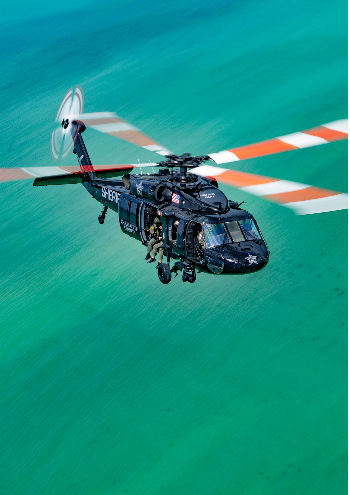 A black helicopter flying over a body of water. Description generated by AI