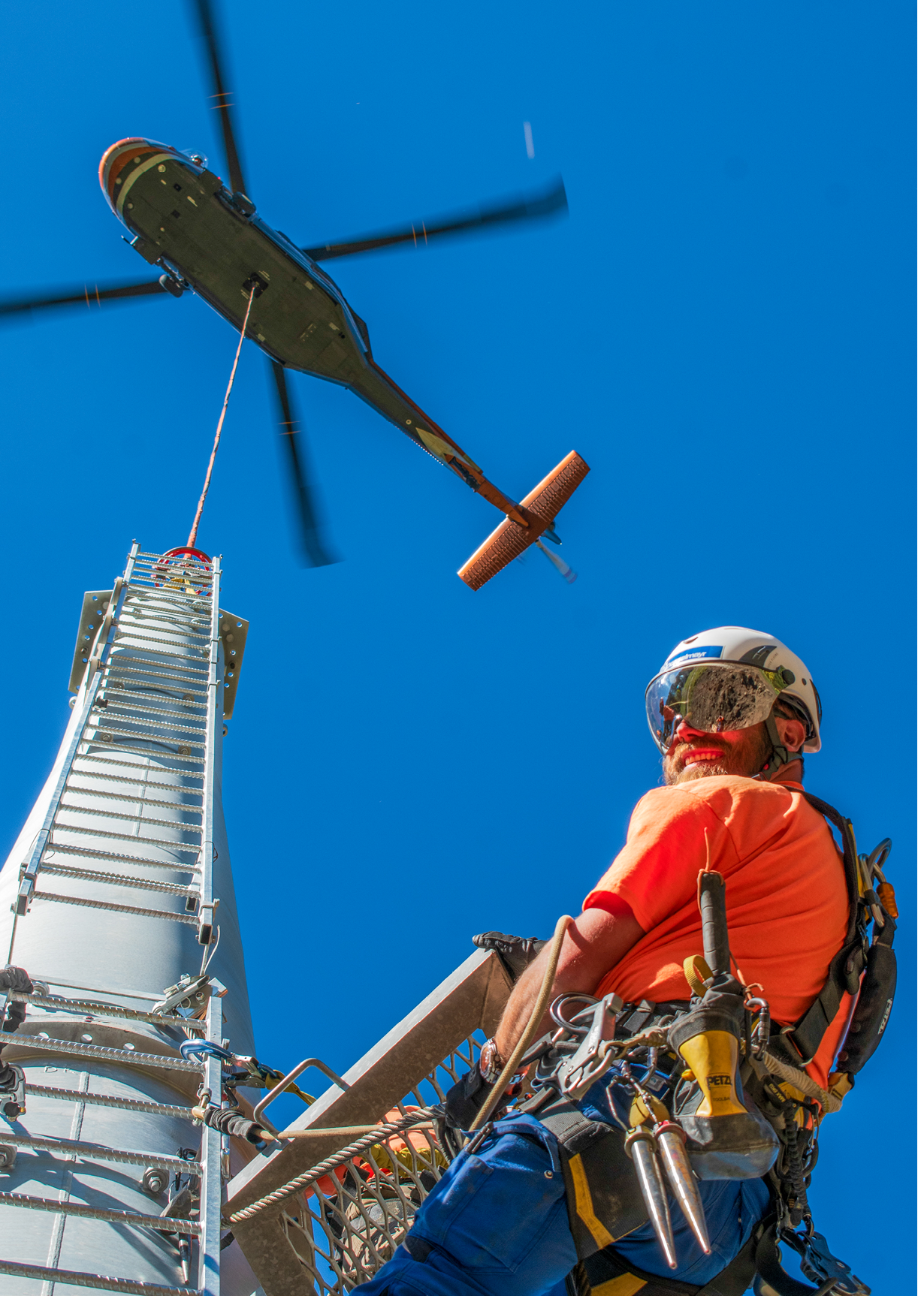 A man wearing a helmet and orange shirt is working on a helicopter. Description generated by AI