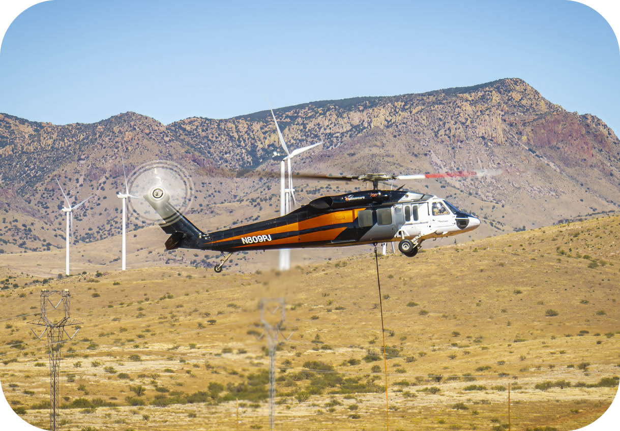 A helicopter flying over a field with windmills in the background. Description generated by AI