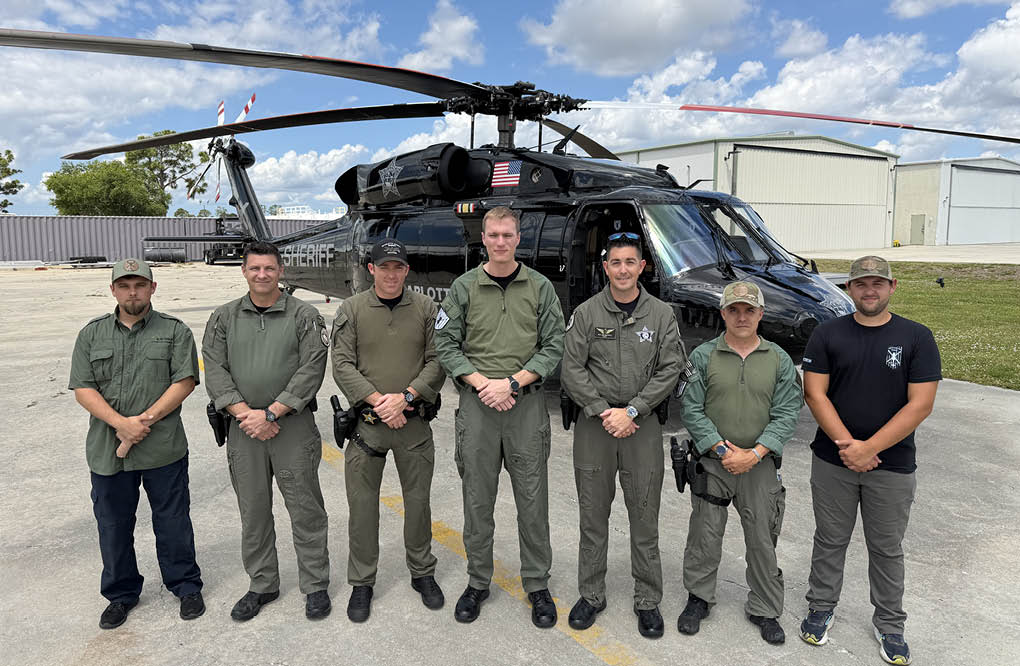 A group of men in uniform standing in front of a helicopter. Description generated by AI