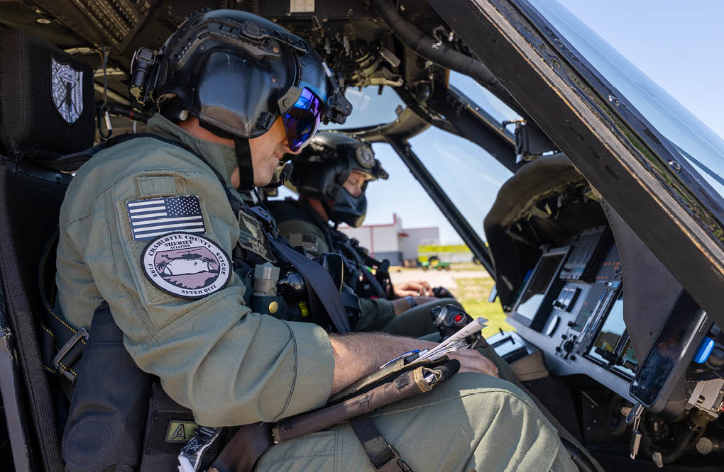 A man wearing a green shirt and a helmet is sitting in a helicopter. Description generated by AI