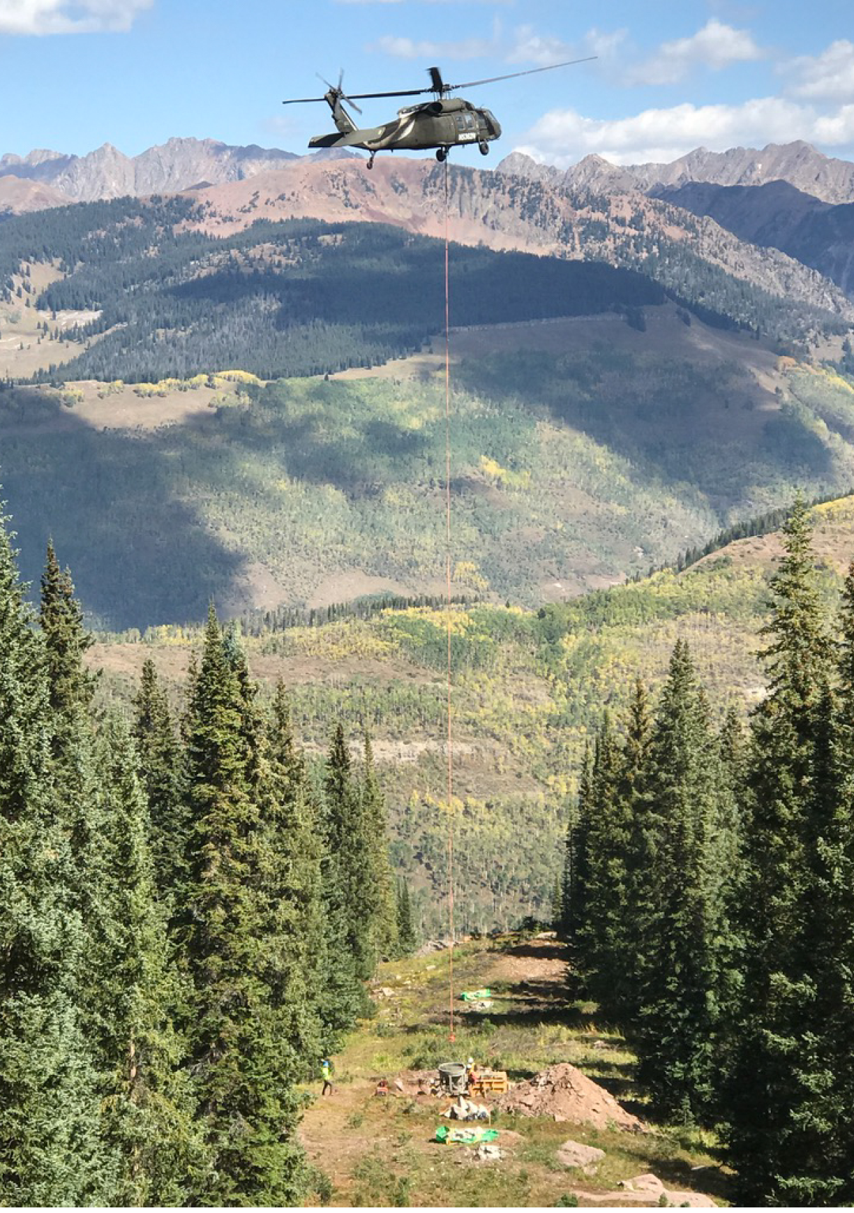 A helicopter is flying over a mountain with a large rope attached to it. Description generated by AI