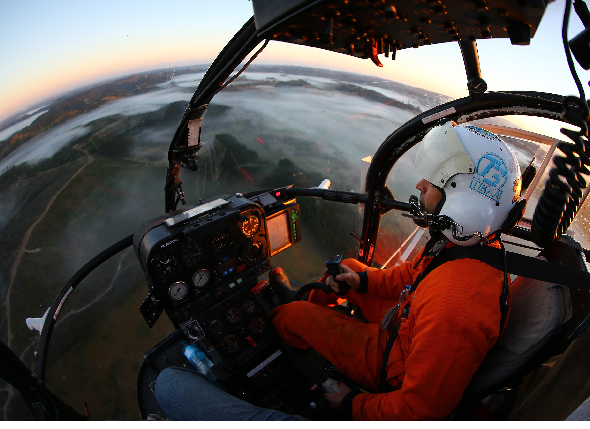 A man wearing an orange shirt is in a helicopter. Description generated by AI