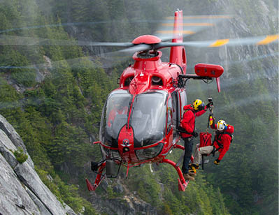 A red and white helicopter flying over a mountain. Description generated by AI