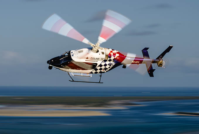 A helicopter with a checkered pattern on it is flying over the ocean. Description generated by AI