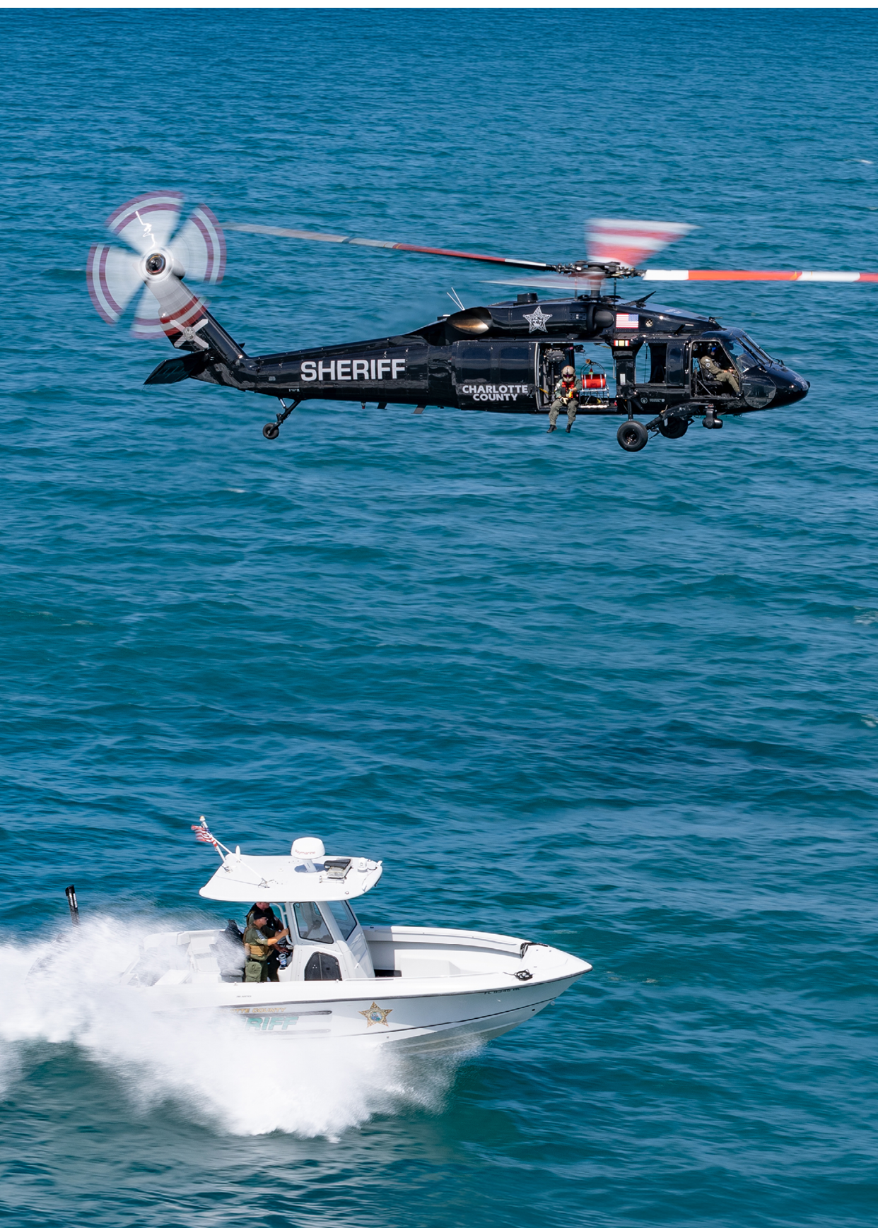 A helicopter is flying above a boat in the ocean. Description generated by AI